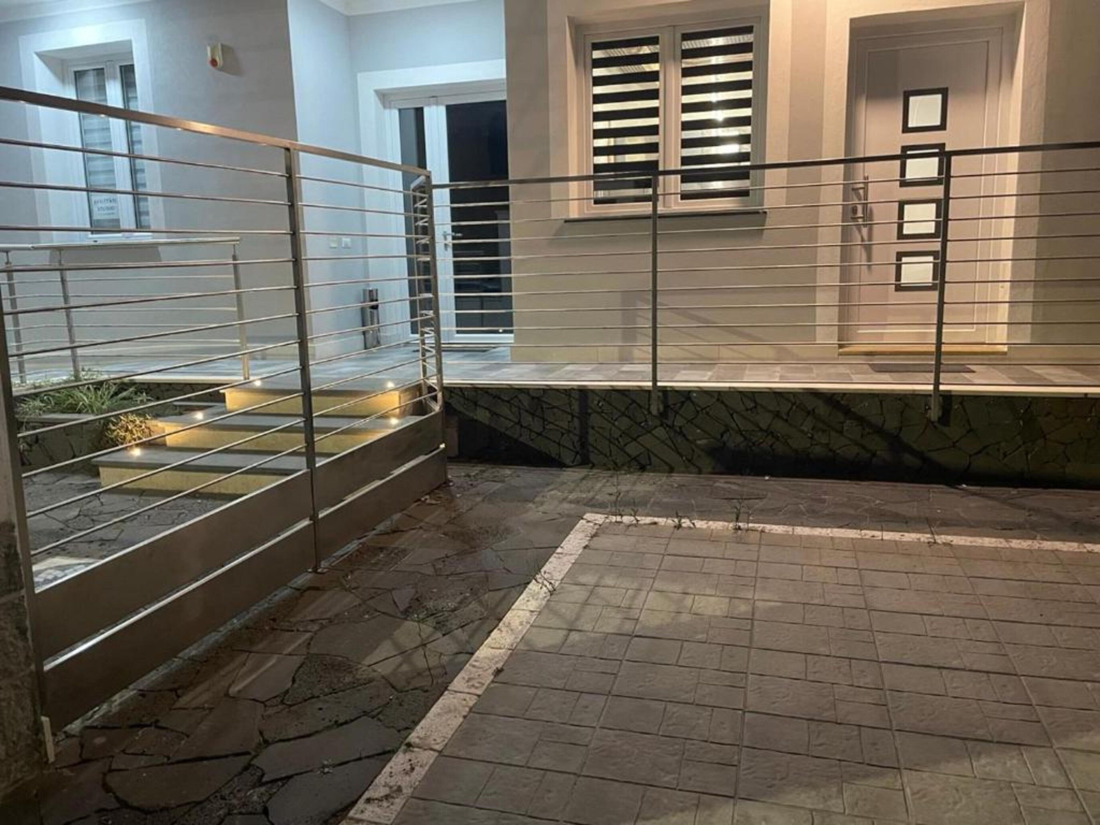 A gated outdoor area with a stone floor, a small water feature, and a building with windows and a door in the background.