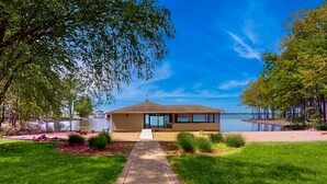 Un chalet au bord du lac, accessible par un sentier qui mène à l’entrée, entouré d’une végétation luxuriante et offrant une vue dégagée sur le lac.