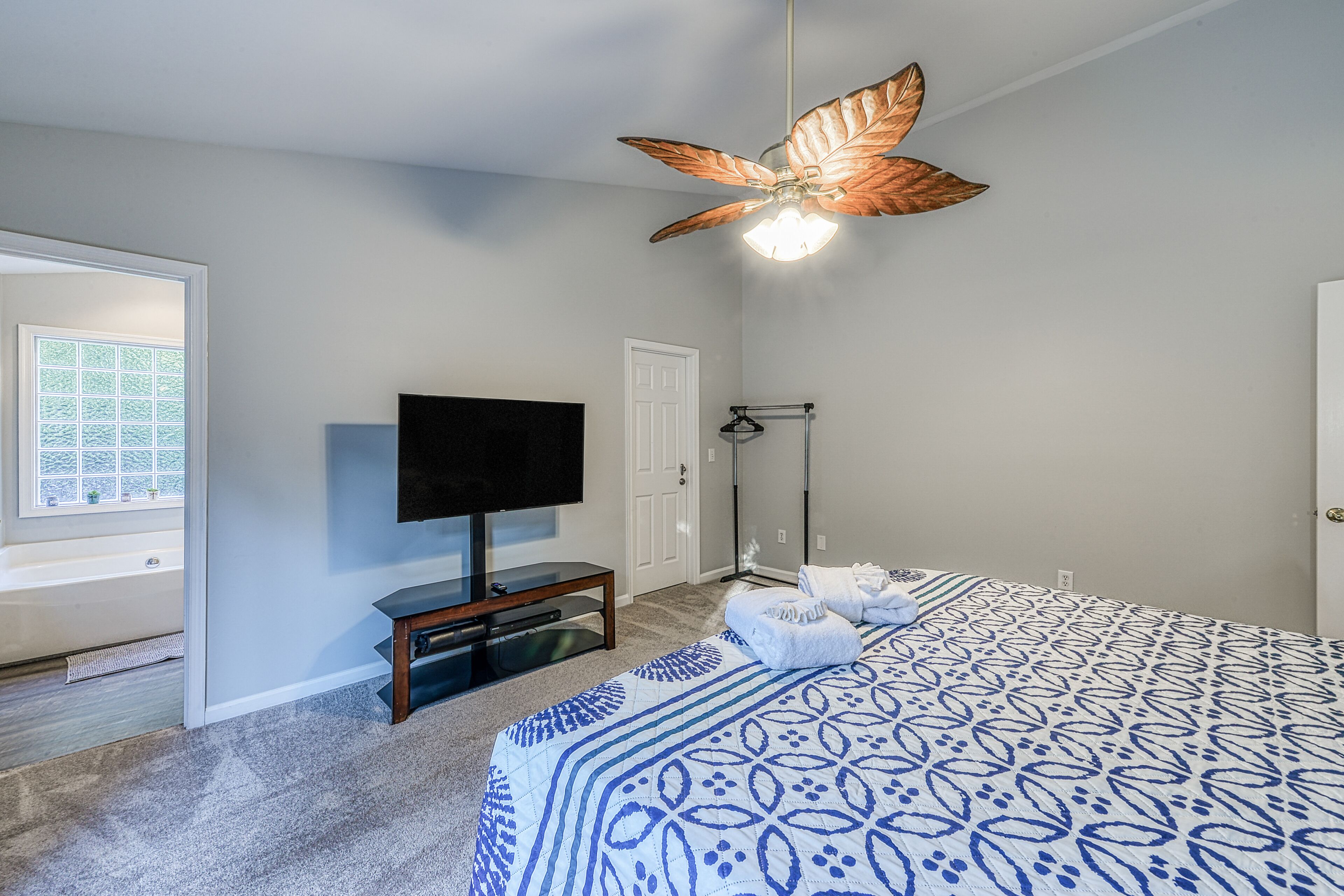 A bedroom with a bed, a ceiling fan, a television, and a window.
