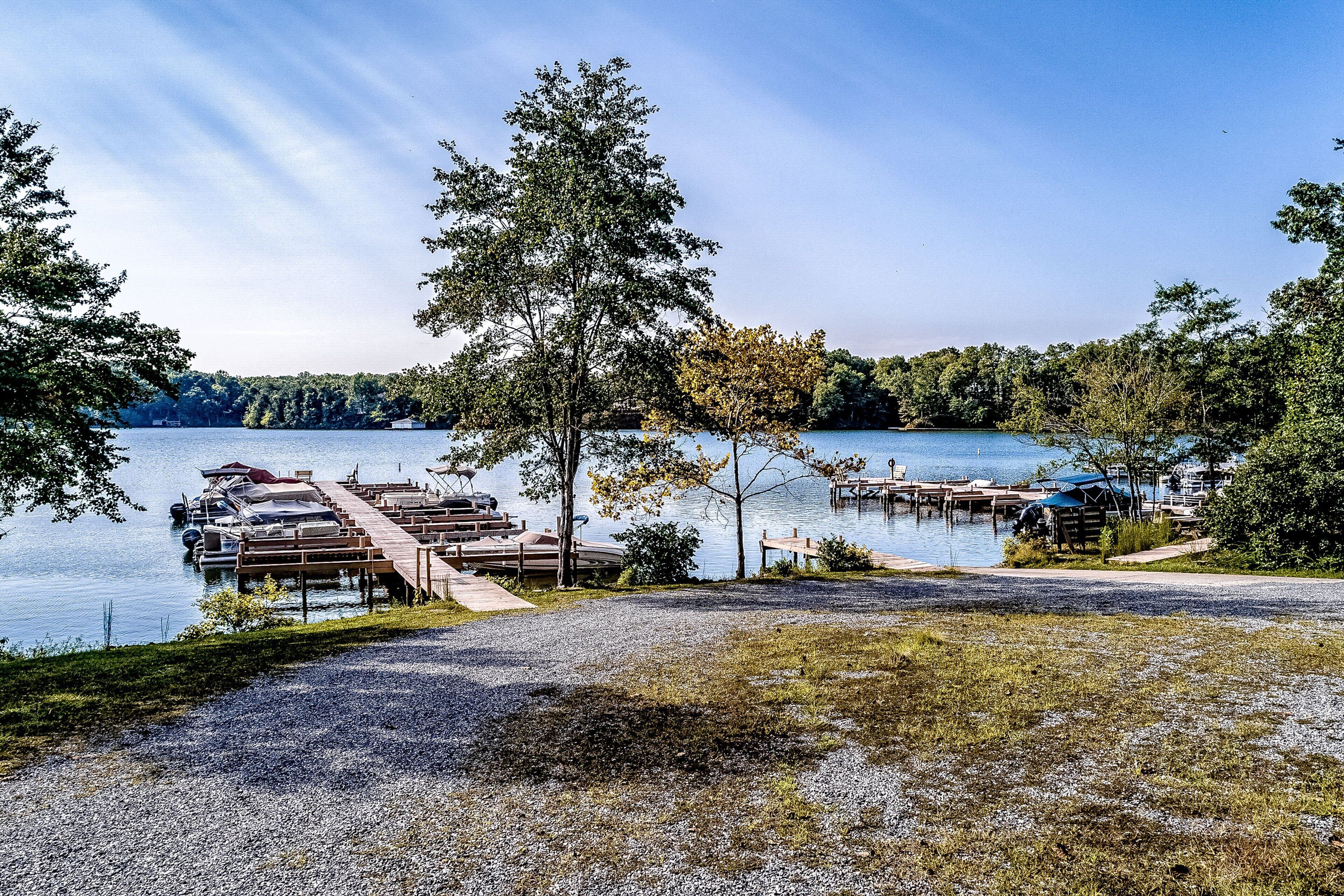 Um cais à beira do lago com barcos, um caminho de cascalho e uma área verde ao fundo.