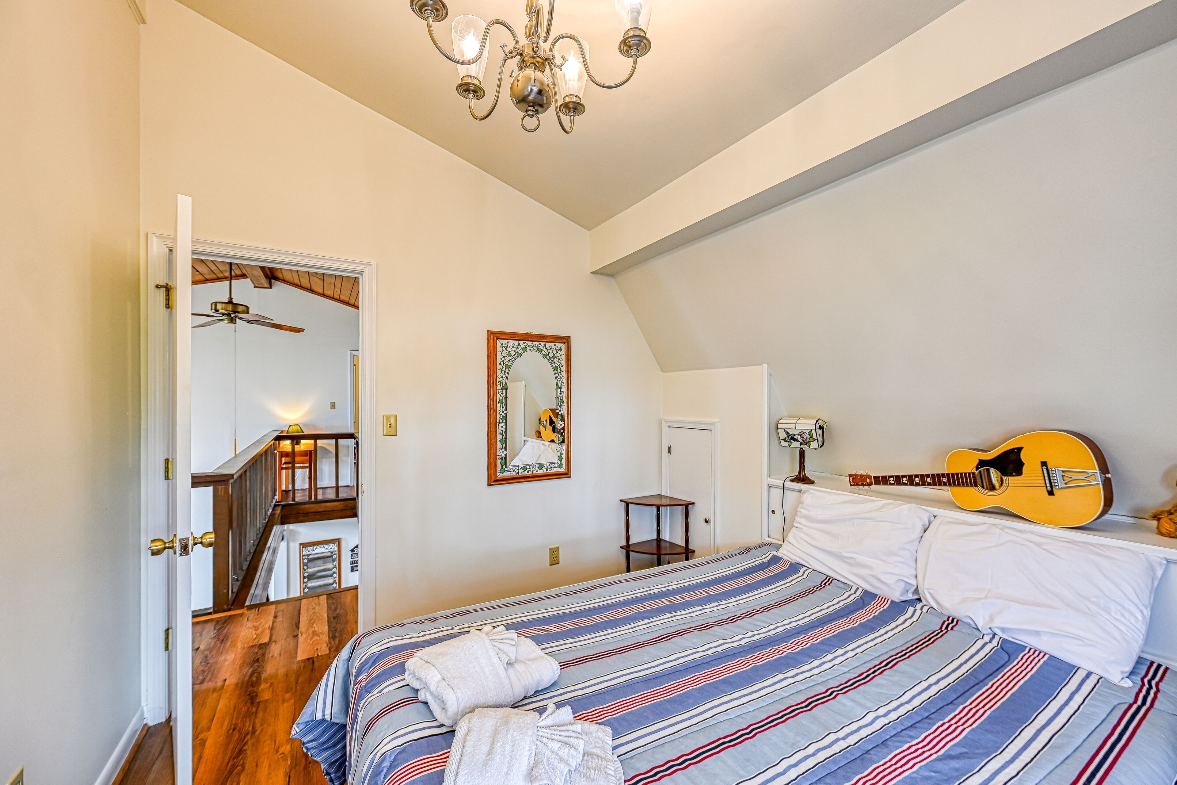 Un dormitorio con una cama, una guitarra, un espejo y una escalera.