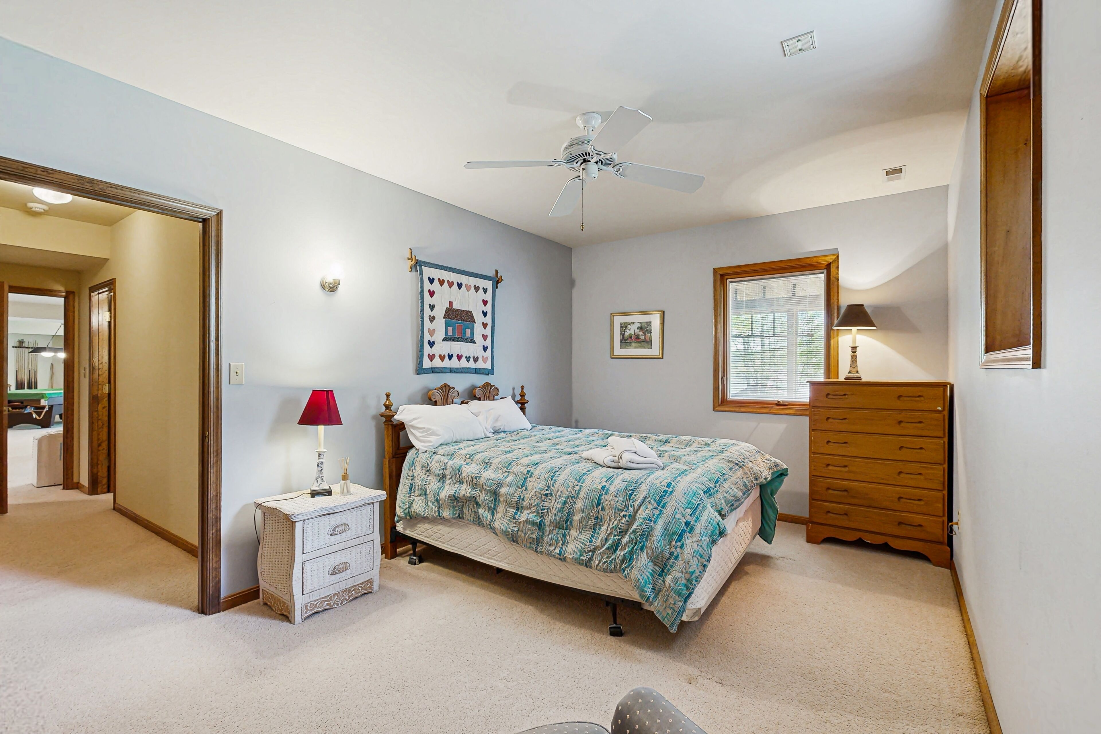 A bedroom with a bed, a nightstand, a dresser, a ceiling fan, and a window.