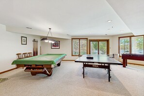 A room with a pool table, a billiards table, and a green felt pool table.