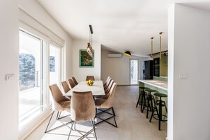 Ein moderner Essbereich mit großem Tisch, mehreren Stühlen und Blick durch große Fenster.