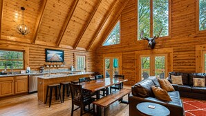 Interior de una cabaña de madera con comedor de madera, cocina y sala de estar con sofá de cuero.