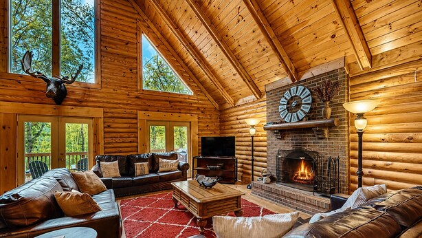 Interior de una cabaña de troncos con chimenea, muebles de cuero y televisor.