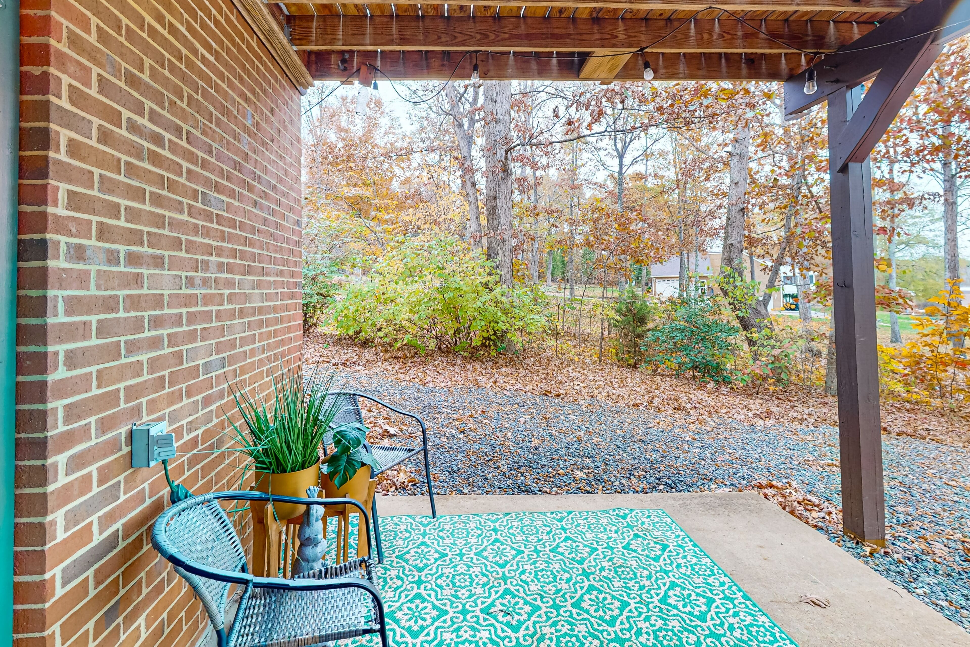 A covered patio with a brick wall, a patterned rug, and a potted plant.