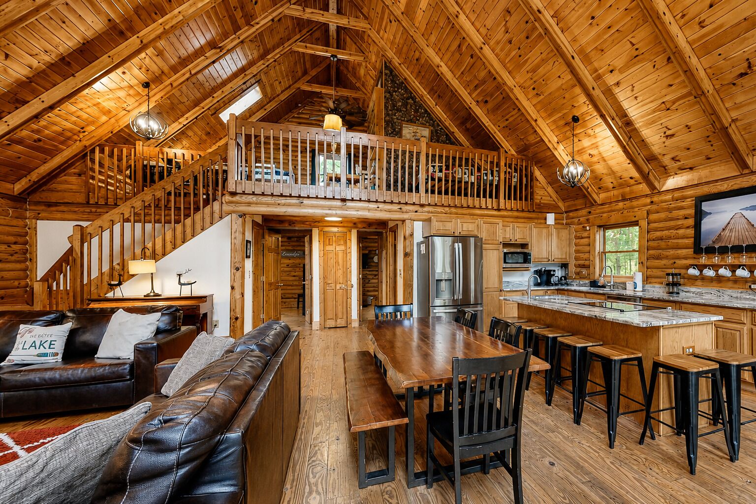 A spacious log cabin with a loft bedroom, a dining area, and a kitchen.