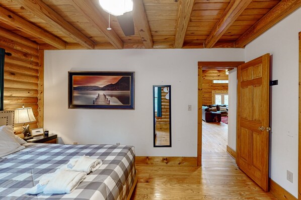 A wooden-paneled room with a bed, a framed picture, a mirror, and a door leading to another room.