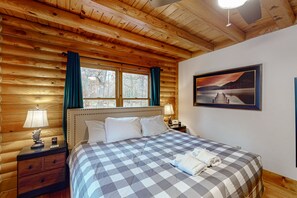Ein schlafzimmer im Chalet-Stil mit karierter Bettdecke, einem gerahmten Landschaftsbild und einer Holzbalkendecke.