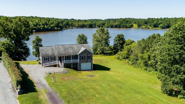 Une maison avec un porche, une pelouse et un lac en arrière-plan.