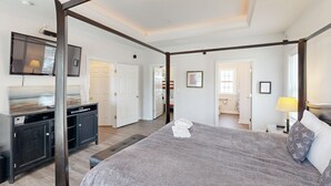 Un lit à baldaquin avec une couvre-lit grise et des serviettes blanches, un bureau en bois foncé avec un téléviseur à écran plat, et un grand miroir au-dessus.
