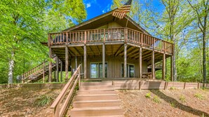 Une cabane en bois dotée d’un balcon, accessible par un escalier, et entourée d’arbres.