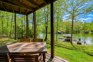 Une terrasse en bois avec une table et des chaises, donnant sur un lac et entourée d’arbres.