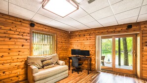 Une pièce chaleureuse aménagée dans un chalet, avec des murs en bois, un canapé, un bureau avec un ordinateur et une porte-fenêtre coulissante donnant sur un espace extérieur.
