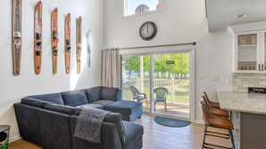 A modern living room with a grey sectional sofa, a kitchen area with a granite countertop, and a balcony with outdoor seating. - Three-story lakefront home w/ covered boat slip, and tennis/pickleball access (Mineral)