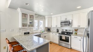 A modern kitchen with white cabinets, granite countertops, stainless steel appliances, and a central island with bar stools. - Three-story lakefront home w/ covered boat slip, and tennis/pickleball access (Mineral)