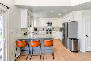 Una cocina moderna con armarios blancos, un refrigerador de acero inoxidable, una encimera de granito y tres taburetes de bar.