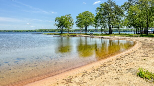 A lakeside view with clear water, sandy beach, and trees. - Three-story lakefront home w/ covered boat slip, and tennis/pickleball access (Mineral)
