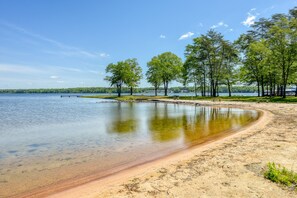 Vista de un lago con agua cristalina, playa arenosa y árboles.