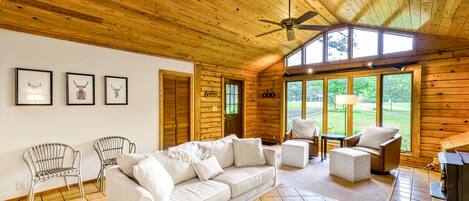 A cozy cabin interior with a wooden ceiling, a sofa set, a dining table, and a fireplace.