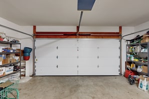 Un garage avec une porte blanche, des étagères remplies de divers objets et un sol en béton.