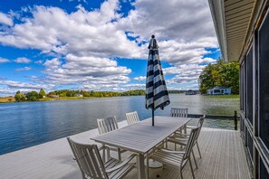 Una terrazza con tavolo e sedie, vista su un lago con una casa sullo sfondo.