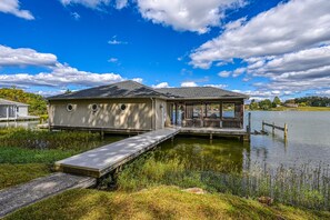 A wooden dock leading to a house with a covered porch, situated by a calm lake. - Beautiful lakefront home with fireplace, deck, central AC, & washer/dryer (Mineral)