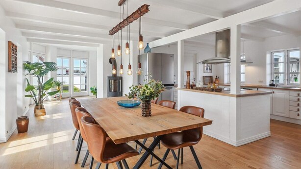 A spacious kitchen with a wooden dining table, modern pendant lights, and a large island. - 4 Star Holiday Home in Blokhus (Blokhus)