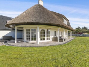 A thatched-roof structure with a covered patio area, white-framed windows, and a grassy lawn. - 4 Star Holiday Home in Blokhus (Blokhus)