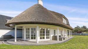 A thatched-roof structure with a covered patio area, white-framed windows, and a grassy lawn. - 4 Star Holiday Home in Blokhus (Blokhus)