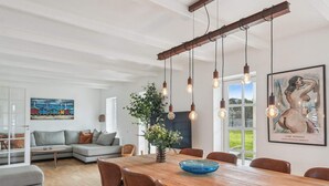 A dining area with a wooden table, brown chairs, hanging light fixtures, and a painting on the wall. - 4 Star Holiday Home in Blokhus (Blokhus)