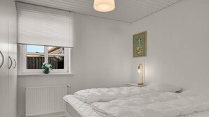 Ein Schlafzimmer mit Bett, Fenster, Heizkörper und einer Wandleuchte.