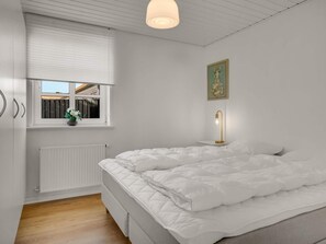 Ein Schlafzimmer mit Bett, Fenster, Heizkörper und einer Wandleuchte.