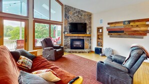A living room with a stone fireplace, a flat-screen TV, and a wooden wall decor. - Spacious lakefront house w/patio, balcony, grill & foosball (Mineral)
