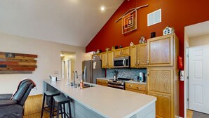 A modern kitchen with wooden cabinets, a large island, and a red accent wall. - Spacious lakefront house w/patio, balcony, grill & foosball (Mineral)