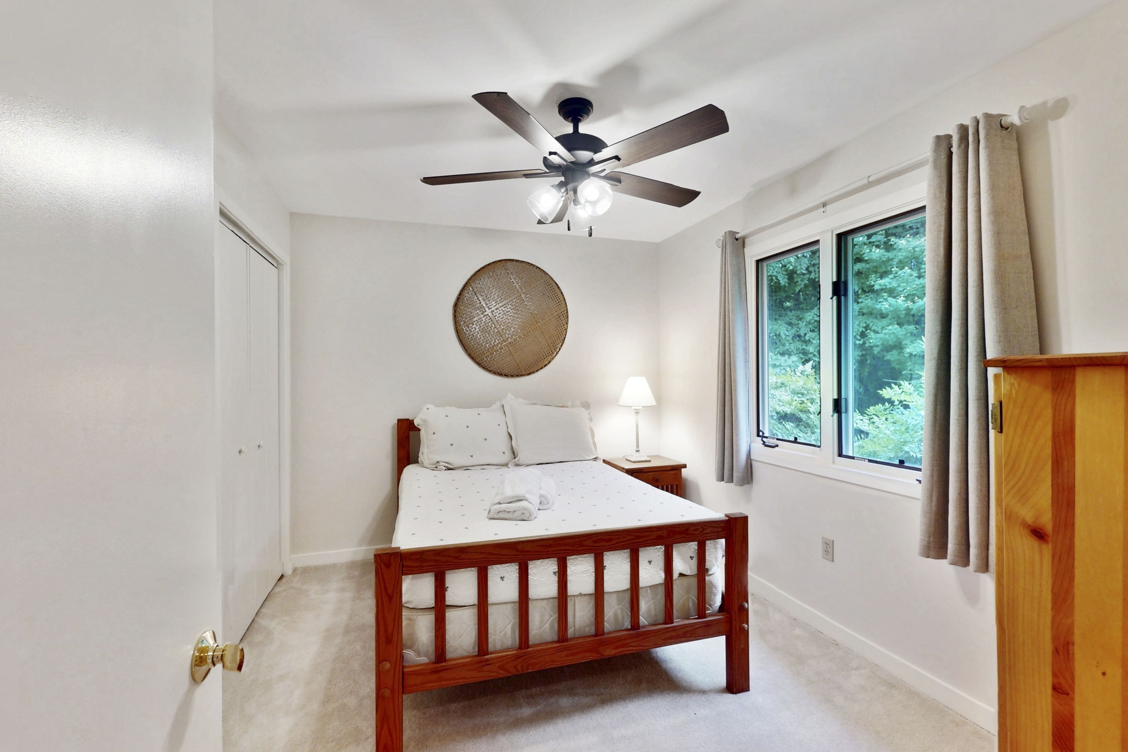 Un dormitorio con cama de madera, ventilador de techo, ventana con cortinas y lámpara de noche.