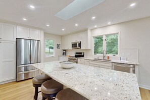 A modern kitchen with white cabinetry, stainless steel appliances, a granite countertop, and a large window. - Spacious waterfront escape with screened porch, water slide, kayak, & games (Mineral)