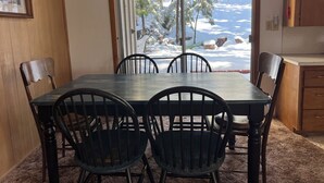 Un comedor con una mesa y sillas, una ventana con vistas a árboles nevados y un armario de madera.