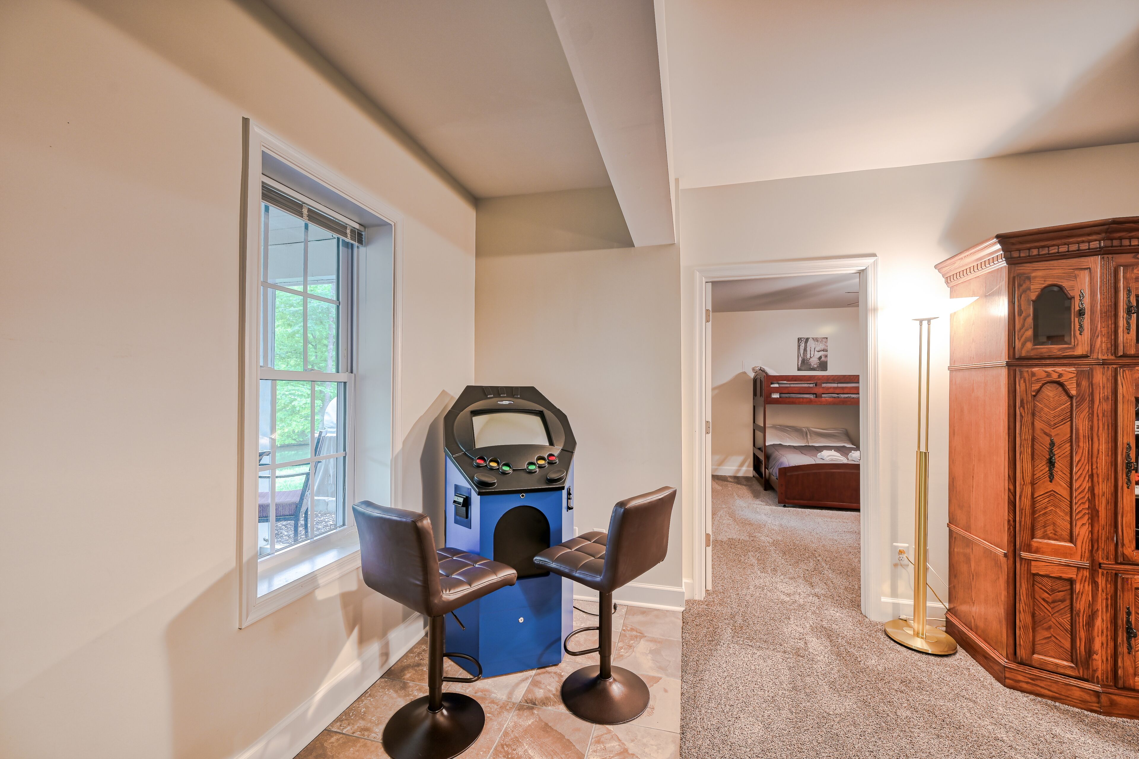 A room with a blue arcade machine, two brown chairs, a wooden cabinet, and a bunk bed in the background.