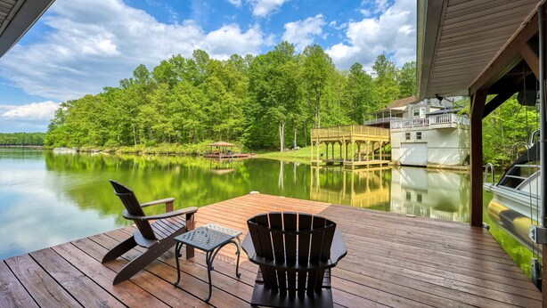 A wooden deck with two Adirondack chairs, a table, and a view of a lake and forest. - Sprawling waterfront home with kayaks, game room, and hot tub (Mineral)