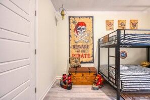 A bunk bed with a striped bedding, a treasure chest, and a pirate-themed wall hanging.