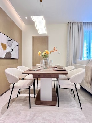 Een moderne eethoek met een rechthoekige tafel, witte stoelen, een vaas met bloemen en een schilderij aan de muur.