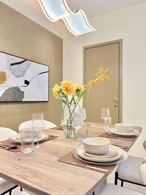 Een moderne eetruimte met een lange tafel, helder servies en een vaas met gele bloemen.