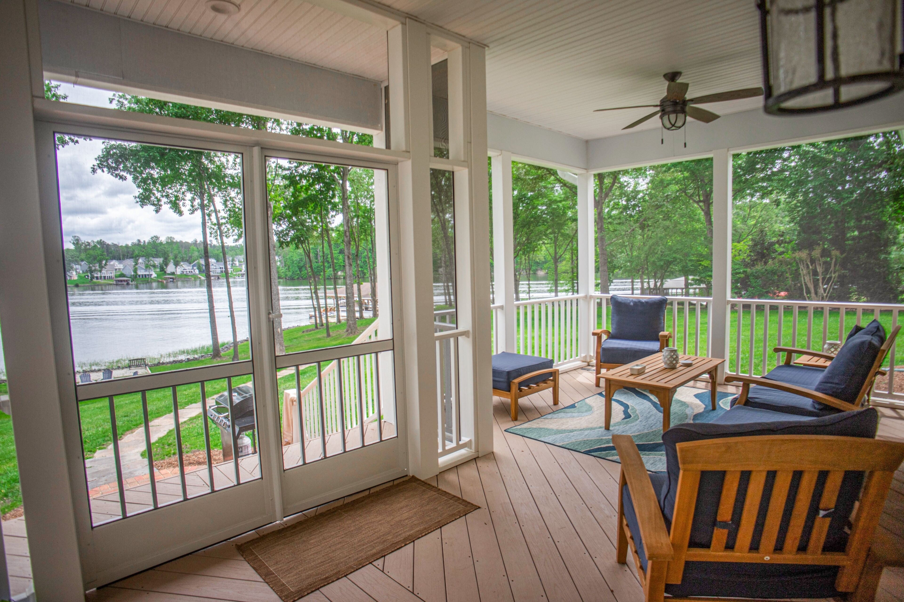 A covered deck with a view of a lake, wooden furniture, and a ceiling fan.
