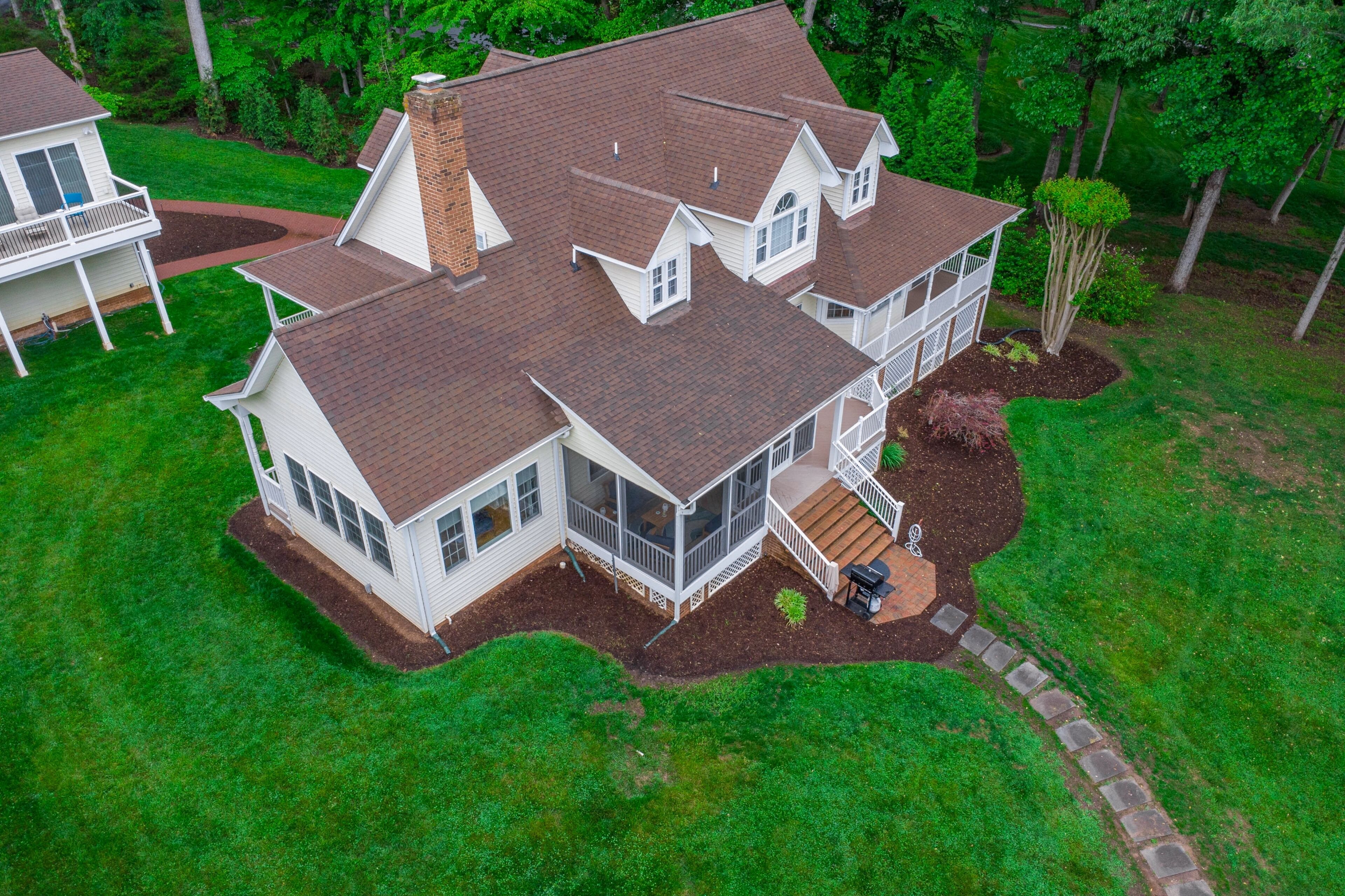 A two-story house with a large deck, a covered porch, and a well-maintained lawn.