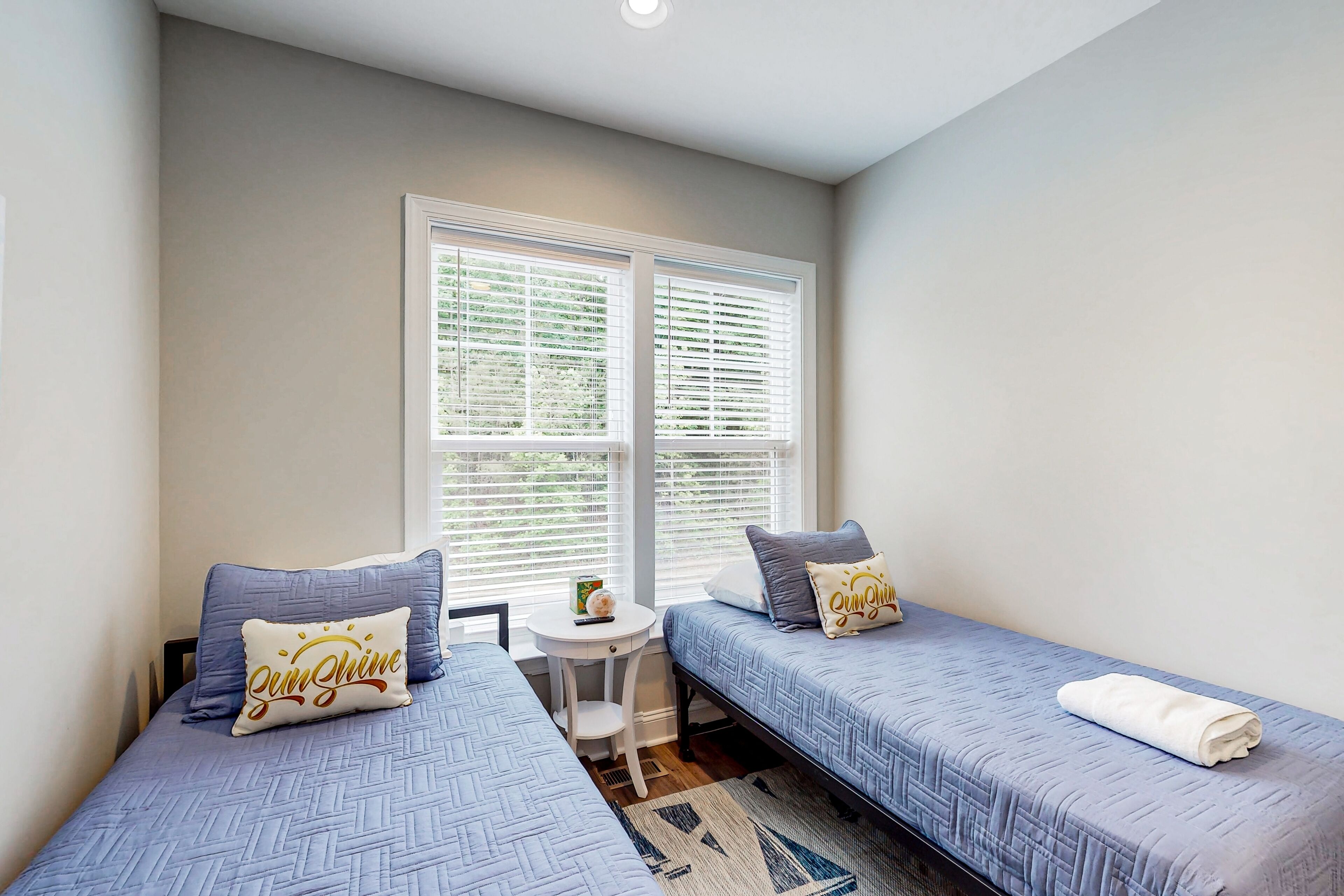 A bedroom with two single beds, a small table, and a window with blinds.