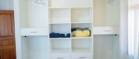 A walk-in closet with open shelving, a hanging rod, and a bed in the foreground.