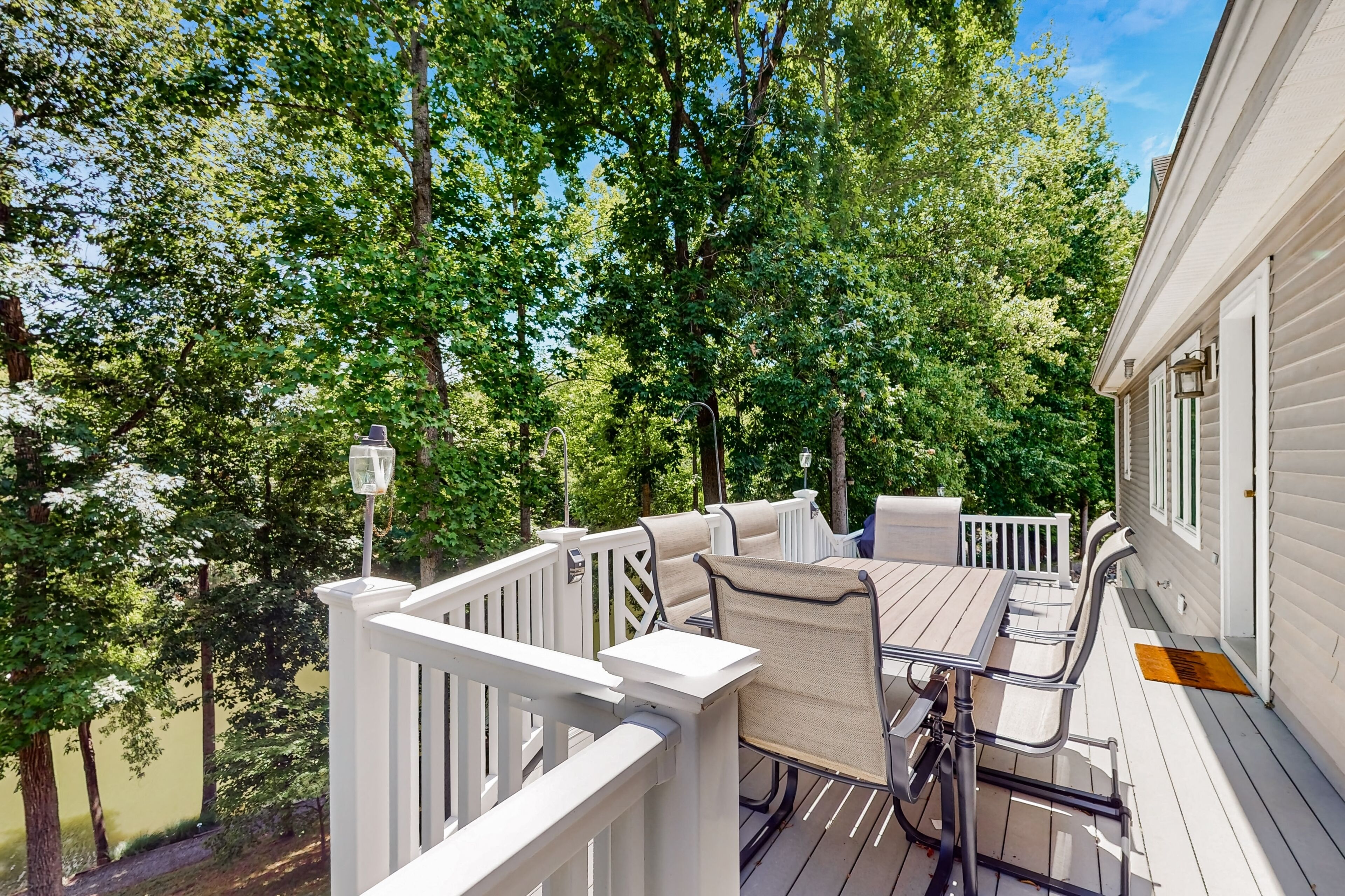 A deck with a table and chairs, surrounded by white railings and trees.