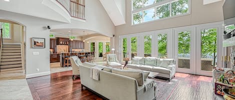 A spacious living area with a high ceiling, large windows, and a staircase leading to an upper level.